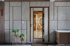 two potted plants sit in front of a door with bamboo panels on the wall