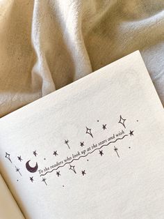 an open book sitting on top of a bed next to a white sheet with stars and moon