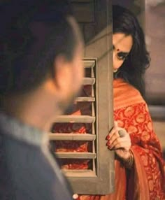 a woman in an orange and red sari is opening the door to another man