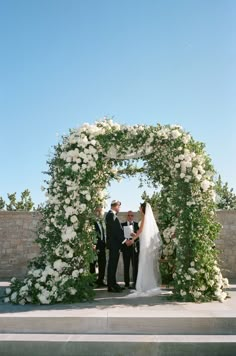 a bride and groom standing under an arch with white flowers on it at their wedding ceremony