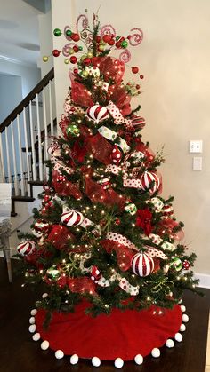 a decorated christmas tree with red and white ornaments on the top, sitting in front of a stair case