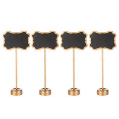 four black and gold place cards on wooden sticks with chalkboard signs in the middle