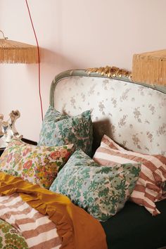 a bed topped with lots of pillows next to a lamp