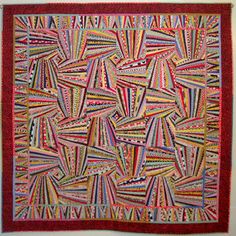 a colorful quilt hanging on the wall in front of a white wall with a red border