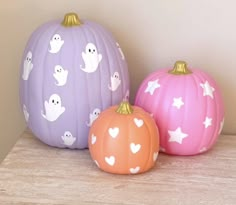 three painted pumpkins sitting on top of a wooden shelf next to eachother