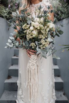 a woman holding a bouquet of flowers and greenery in front of her face on some steps