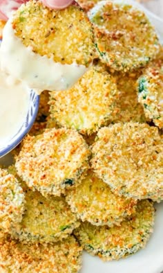 a person dipping something into a bowl of dip on top of some fried broccoli