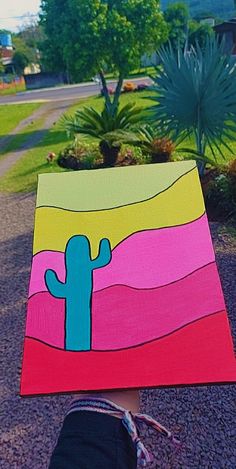 a person holding up a colorful piece of art with a cactus painted on it's side