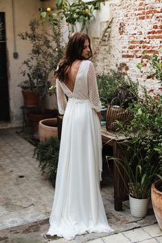 a woman standing in front of a brick wall wearing a white dress with long sleeves