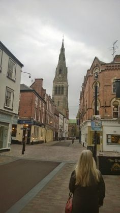 a woman is walking down the street in front of some buildings and a clock tower