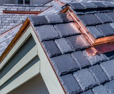 the roof of a house with slate shingles and copper flashings on it's windows