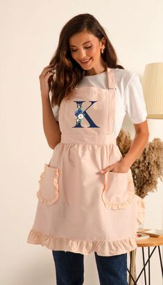 a woman wearing an apron with the letter k on it, standing in front of a chair