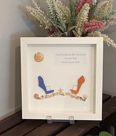 a vase filled with flowers sitting on top of a wooden table next to a white frame