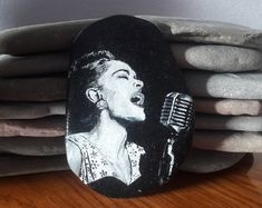 a rock with a painting of a woman singing into a microphone on top of some rocks