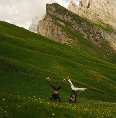 two people are playing in the grass on a mountain