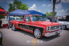 an old red pickup truck parked in a parking lot next to other cars and tents