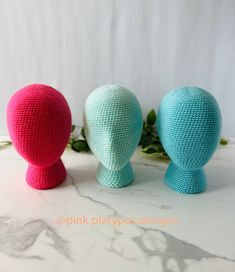 three crocheted eggs sitting next to each other on a table with greenery