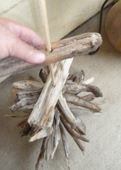 a person holding a stick over some driftwood on the floor next to a potted plant