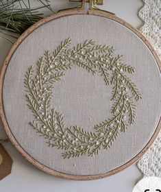 an embroidery hoop with a wreath on it next to some pine needles and other items