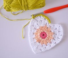 a crocheted heart next to a ball of yarn and a knitting needle on a white surface