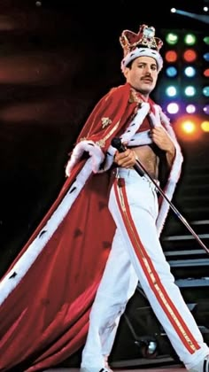 a man dressed in white and red with a crown on his head walking across a stage