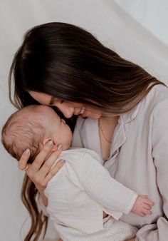 a woman holding a baby in her arms and kissing it's face with both hands