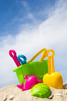 there are some toys in the sand on the beach and one is pink, green, blue, yellow