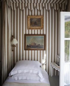 a bedroom with striped walls and white linens on the bed, framed by an antique painting