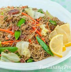 a white plate topped with noodles and veggies next to a lemon wedged slice