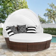 an outdoor day bed with black and white pillows next to a swimming pool in the background