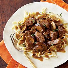 a white plate topped with pasta and meat covered in sauce on top of a wooden table