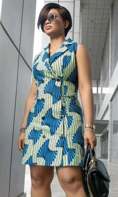 a woman in a blue and green dress holding a black purse standing next to a building