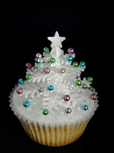 a cupcake decorated with white frosting and multicolored decorations on top, sitting in front of a black background