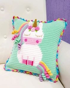 a pillow with a crocheted unicorn on it sitting on a white chair next to a purple wall