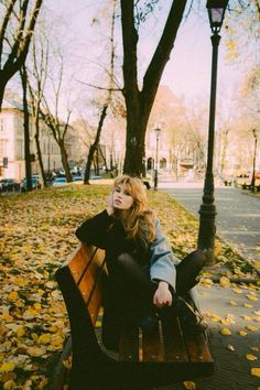 a woman sitting on top of a wooden bench next to a lamp post and tree