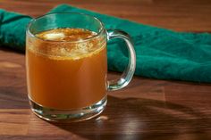 a glass mug filled with liquid sitting on top of a wooden table next to a green towel