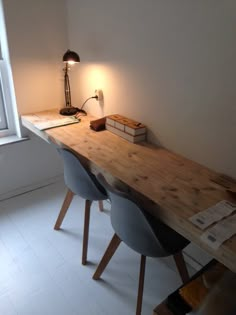 a wooden desk with two chairs and a lamp on top of it in front of a window