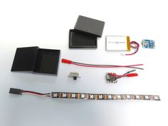 electronic components displayed on white surface with red wires and other items around them, including an analog clock