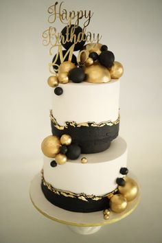 a three tiered white and black cake with gold decorations on the top, happy birthday