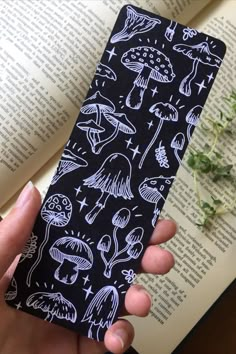 a hand holding an iphone case with white ink on black paper that has different types of mushrooms