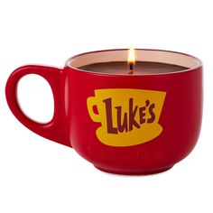 a red coffee cup with a lit candle in it's center that says luke's