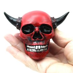 a hand holding a red skull with horns on it