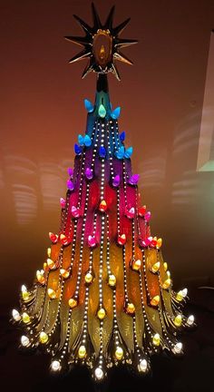 a multicolored christmas tree made out of wine bottle caps and lights with a sun on top