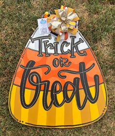 a trick or treat sign laying in the grass with a bow on it's head