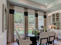 a dinning room table and chairs in front of two windows with curtains on them