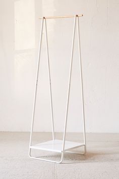 a white shelf sitting on top of a cement floor next to a wall with a wooden stick sticking out of it