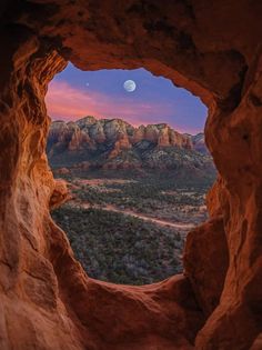 the moon is seen through an opening in a rock formation with mountains in the background