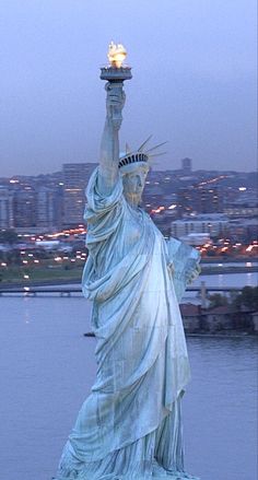 the statue of liberty is lit up at night in front of a cityscape