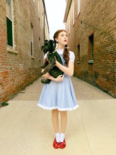 a girl in a blue dress holding a small dog and looking up at the sky