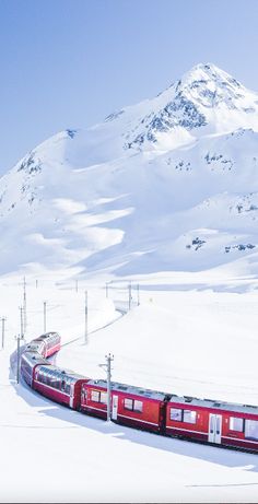 a red train traveling down tracks next to a snow covered mountain in the wintertime